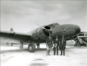 Three men standing in front of an airplane parked at an airfield